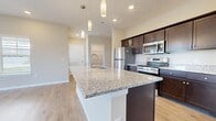 This well-appointed single-floor home in Maumee, Ohio offers a generous layout across two bedrooms, one bathroom, and multiple closets, providing ample storage throughout. The open-concept kitchen and living area serves as the heart of the home, anchored by a large granite-topped island with an undermount sink and elegant pendant lighting overhead. Rich dark cabinetry pairs with stainless steel appliances, including a refrigerator, range, and microwave, while light hardwood-style flooring extends throughout the main living areas, creating a cohesive and bright atmosphere. The living room benefits from vaulted ceilings and large windows that invite abundant natural light and outdoor views. Both bedrooms feature plush carpeting, ceiling fans, and generous window coverage, with the primary bedroom offering two windows and a dedicated closet. The bathroom echoes the kitchen's design sensibility, with a dark vanity topped with granite counters, a large mirror, and light flooring. Three closets distributed throughout the home ensure practical storage. The overall aesthetic is clean, contemporary, and move-in ready.