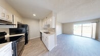 This single-story unit presents a clean, functional layout designed for comfortable everyday living. The galley-style kitchen is well-appointed with white cabinetry offering ample storage, light countertops, a stainless steel sink, and black appliances including a range, refrigerator, and dishwasher. Light wood-look flooring runs throughout the kitchen and connects seamlessly to the adjoining living and dining areas.

The living space is generously sized, featuring neutral-toned walls, a textured ceiling, and a sliding glass door that invites natural light and provides outdoor access. An additional open living area is visible from the kitchen, reinforcing the unit's open and connected feel.

The bedroom is carpeted for added comfort and includes a ceiling fan, a window with natural light, and a reach-in closet with bifold doors. A separate closet space is also noted in one of the main living areas, providing additional storage flexibility.

The bathroom features wood-look flooring, a tub-shower combination with white tile surround, a white vanity with countertop, and a mirror. Throughout the unit, the consistent use of neutral tones and updated finishes creates a bright, cohesive atmosphere.