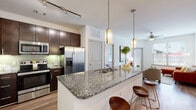 This well-designed single-floor residence offers a thoughtfully laid-out open-concept floor plan with contemporary finishes throughout. The kitchen serves as a central highlight, showcasing rich dark-wood cabinetry, granite countertops, stainless steel appliances including a French door refrigerator, electric range, and built-in microwave, complemented by a green tile backsplash and under-cabinet lighting. A large kitchen island with granite countertops provides bar seating and additional workspace, illuminated by elegant pendant lighting and a track lighting system above.

The living area features warm wood-look flooring, a ceiling fan, and large windows that invite ample natural light and outdoor views. The space flows seamlessly from the kitchen and dining areas, creating an inviting, connected atmosphere.

Both bedrooms are bright and comfortable, each featuring wood-look flooring, ceiling fans, and well-sized windows. The bathrooms are finished with granite-topped dark-wood vanities, framed mirrors, and modern fixtures. The primary bathroom offers a spacious walk-in closet and a glass-enclosed shower, while a secondary bathroom provides equally refined finishes. Throughout the residence, consistent use of neutral tones, quality materials, and thoughtful lighting create a cohesive and polished living environment.