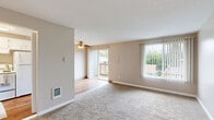 This single-floor, 3-bedroom, 1-bathroom residence offers a practical and well-organized layout designed to maximize every square foot. The open living and dining area is bathed in natural light courtesy of large sliding glass doors that lead to a private outdoor deck, as well as a broad window fitted with vertical blinds. A ceiling fan adds comfort to this shared space, which features neutral-toned carpet and warm beige walls throughout. The transition from the carpeted living area to the kitchen is marked by hardwood flooring, lending the space a pleasant material contrast. The compact kitchen is thoughtfully equipped with white cabinetry, a full-size refrigerator, a dishwasher, and a stainless sink, all illuminated by a flush-mount ceiling fixture. Each of the three bedrooms is finished with plush carpet and features windows that invite natural light and views of the surrounding greenery. Baseboard heating units ensure consistent warmth. The full bathroom includes a tub-shower combination with a handheld showerhead, a vanity with light countertops, white cabinetry, and hardwood flooring. Clean white trim and a consistent neutral palette throughout the unit create a cohesive, move-in-ready atmosphere.