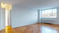 This single-floor residence is defined by its warm, classic parquet wood flooring that extends throughout the living areas and bedrooms, lending a timeless character to the interior. The open living area is bathed in natural light through large windows fitted with horizontal blinds, offering views of the surrounding urban landscape. A sliding glass door provides direct access to an outdoor balcony, further connecting the interior to the city beyond. A baseboard heating unit is positioned beneath the main window, ensuring year-round comfort.

The kitchen is efficiently designed with light wood cabinetry, white quartz countertops, a stainless steel sink, and a full suite of stainless steel appliances including a refrigerator, gas range, microwave, and dishwasher. Large-format white tile flooring completes the clean, contemporary look of this space.

The bedroom is well-proportioned, featuring its own window with natural light and urban views, parquet flooring, and a notable double set of built-in closets with louvered bifold doors, offering substantial storage and organizational capacity.

The bathroom is appointed with an elegant marble vanity countertop and undermount sink, white subway tile walls, a mirrored medicine cabinet, terrazzo flooring, and a combined shower and tub — delivering a refined, classic aesthetic throughout.