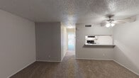 Located at 4322 Kostoryz Rd in Corpus Christi, Texas, this single-story unit offers a practical and functional layout across its living spaces. The open living area is finished with wall-to-wall carpeting and features a ceiling fan with light, a textured popcorn ceiling, and neutral gray walls that create a clean, understated ambiance. A hallway connects the main living area to the rest of the unit, with a glimpse of natural light visible at the far end. The front entry opens into the carpeted living room, which includes a window for added natural light.

The kitchen is accessible via a pass-through counter that opens to the living and dining area, offering a sense of connectivity between spaces. White cabinetry, speckled laminate countertops, light wood-look vinyl flooring, and black appliances — including a full-size refrigerator and range — complete the kitchen. The layout provides a clear sightline through to the bathroom beyond.

The bedroom is a well-proportioned, carpeted room with a ceiling fan and light fixture, neutral walls, and a sliding glass door fitted with vertical blinds that leads to an outdoor patio area with exterior views. The bathroom includes a full tub and shower combo with white tile surround, a chrome curtain rod, and wood-look vinyl flooring, maintaining a clean and functional aesthetic throughout.