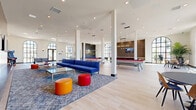 Located at 1900 E Inland Empire Blvd in Ontario, California, this single-floor community amenity space offers a generously sized, open-plan layout designed for recreation and socializing. The interior is defined by soaring ceilings supported by white structural columns, and an abundance of natural light streaming through dramatic arched, floor-to-ceiling windows with black steel frames that line the perimeter walls.

Light hardwood flooring extends throughout the entire space, lending a clean, contemporary aesthetic. The main game and recreation area features multiple billiard tables with vibrant red felt, a ping-pong table, foosball, and classic arcade machines — all thoughtfully arranged to maximize flow and usability. A dedicated lounge zone anchors the center of the space with a bold blue sectional sofa, colorful ottomans, and a glass coffee table atop a patterned area rug, complemented by a wall-mounted flat-screen TV.

A standout wet bar area showcases a dramatic dark marble waterfall-edge island, wood cabinetry, glossy textured tile backsplash, and elegant pendant lighting — ideal for hosting events. Dining tables with modern chairs are positioned near the windowed walls to take advantage of the outdoor views. Recessed lighting and pendant fixtures provide warm, even illumination throughout, completing this vibrant, well-appointed gathering space.
