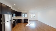 This two-floor residence is thoughtfully designed with a clean, modern aesthetic carried consistently throughout both levels. The main living area is open-concept, combining the kitchen and living space into one expansive, light-filled room. Large black-framed windows allow natural light to flood the space, reflecting off warm-toned hardwood flooring. The kitchen is well-appointed with bold dark cabinetry, white countertops, and a full suite of stainless steel appliances including a gas range, built-in microwave, dishwasher, and refrigerator. A stacked washer and dryer unit is conveniently integrated into the main floor, alongside additional storage cabinetry.

The bathroom features a white vanity with a square undermount sink, a large mirror, and a tub-shower combination with sliding glass doors. Bedrooms are carpeted and receive natural light through black-framed windows with outdoor views of surrounding greenery.

The two floors are connected by a wood-tread staircase with warm-toned handrails on both sides and recessed overhead lighting. An exit route sign is clearly posted near the stairwell entry. Throughout the space, recessed lighting, white walls, and clean trim work contribute to a bright, contemporary atmosphere.