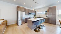 Located in Draper, Utah, this contemporary multi-floor home offers a well-designed layout spread across three levels. The entry level provides a welcoming introduction to the space, while the main floor serves as the heart of the home, featuring an open-concept living room, dining area, and kitchen. The living room is bright and airy, with light hardwood flooring, recessed lighting, and French doors that open to an outdoor area, inviting natural light throughout. The kitchen is equipped with warm taupe shaker cabinetry, white quartz countertops, stainless steel appliances, and a undermount sink — combining functionality with a clean, modern aesthetic. The dining area benefits from large windows with views of the surrounding neighborhood. Upstairs, two well-proportioned bedrooms offer comfortable retreats, each featuring light hardwood floors, ample natural light, and closet space. A dedicated office with a ceiling fan and large window provides an ideal workspace. The home includes three full bathrooms: one features a glass-enclosed walk-in shower with large-format tile, while another offers a soaking tub and shower combination — both finished with gray wood-tone vanities and white countertops. Consistent light hardwood flooring and a neutral color palette tie the entire home together in a cohesive, modern style.