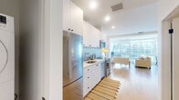 Located on Wilshire Boulevard in the heart of Los Angeles, this thoughtfully designed studio offers a modern, efficient layout across a single floor. The open-plan kitchen and living area is bathed in natural light from expansive floor-to-ceiling windows, which frame striking views of the surrounding cityscape. Light hardwood flooring runs throughout, lending warmth and continuity to the space.

The kitchen is outfitted with sleek white cabinetry extending to the ceiling, a textured tile backsplash, light quartz countertops, and a full suite of stainless steel appliances including a refrigerator, range, microwave, and dishwasher. The living area accommodates comfortable seating and a dining setup, all oriented to take full advantage of the panoramic urban views.

The bathroom is clean and contemporary, featuring a white vanity with quartz countertop, tiled tub-shower combination, and neutral tile flooring. A generously sized walk-in closet provides ample storage with built-in shelving units and multiple hanging rods along the walls. The overall ambiance of the space is bright, modern, and urban, making it a well-appointed residence in one of Los Angeles's most prominent corridors.