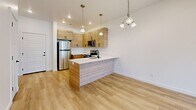 This well-designed three-bedroom, two-bathroom home in Lehi, Utah offers a clean, modern aesthetic throughout its single-floor layout. The open-concept kitchen and living area serves as the heart of the home, featuring light wood cabinetry with matte black hardware, white quartz countertops, a peninsula with an undermount sink, and a full suite of stainless steel appliances including a refrigerator, electric range, and microwave. Pendant lighting and a chandelier add warmth to the space, which flows seamlessly into a bright living area with light hardwood-style flooring and recessed lighting. A sliding glass door opens to a private balcony, allowing natural light to fill the room. The two bathrooms maintain the same cohesive design language, with wood-tone vanities, white quartz counters, and matte black fixtures set against light hardwood-style flooring and crisp white walls. The three bedrooms feature soft carpet flooring and bright windows with blinds that invite natural light. Four closets provide ample storage throughout the home. The overall ambiance is bright, clean, and contemporary, reflecting a fresh, move-in-ready feel.