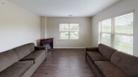 This single-floor residence offers a functional and thoughtfully designed layout that balances comfort with practicality. The living room serves as the heart of the home, featuring rich dark hardwood-style flooring, neutral warm-toned walls, and a classic wood-mantle fireplace that adds character and coziness to the space. Multiple windows fitted with horizontal blinds allow generous natural light to flow in while maintaining privacy, with views of the surrounding greenery outside.

The kitchen is well-equipped and efficiently laid out in a U-shaped configuration, featuring cream-toned cabinetry with brushed hardware, granite-look countertops, a stainless steel refrigerator, an electric stovetop, and a double basin sink positioned beneath a window. A peninsula counter extends the workspace and provides an open connection to the adjacent dining or living area, while a pendant light overhead adds a refined touch.

The bedroom is a serene and simply appointed retreat, with the same dark hardwood-style flooring continuing throughout, neutral walls, and a large window with vertical blinds that invites ample daylight.

The bathroom is designed with accessibility in mind, equipped with sturdy grab bars near the toilet, a granite-topped vanity, and tile flooring. An adjacent walk-in closet provides generous storage space, completing this practical and comfortable home.