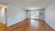 Located at 2005 NE Terre View Dr in Pullman, WA, this two-bedroom, one-bathroom unit offers a practical and well-organized single-floor layout. The living room is a bright, open space featuring wood-look laminate flooring, a baseboard heating system, a wall-mounted air conditioning unit, and a sliding glass door that fills the room with natural light and provides access to an outdoor balcony area. The kitchen is efficiently designed with white cabinetry, light countertops, a window above the sink, and black appliances including a range, dishwasher, and refrigerator, all set on matching laminate flooring. Both bedrooms are carpeted in warm-toned plush carpet with light gray walls, textured ceilings, and windows that allow in natural light. The primary bedroom offers a generous footprint with direct access to the full bathroom, which features a tiled tub-shower combination and clean, white finishes. The second bedroom includes a closet and connects conveniently to the hallway. Baseboard heaters are present throughout the unit, ensuring consistent climate control. The overall aesthetic is clean and neutral, providing a functional living environment in the heart of Pullman.
