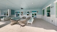 This upscale property in Fort Myers, Florida, offers a resort-like experience with its impressive amenities. The centerpiece is a large, rectangular swimming pool surrounded by ample deck space furnished with numerous lounge chairs for sunbathing. Palm trees line the poolside, creating a tropical ambiance. 

The complex features multiple four-story buildings painted in a soothing light blue, complementing the Florida sky. These structures house residential units, likely apartments or condominiums, with balconies offering views of the grounds.

A covered lounge area showcases a coastal-inspired design with light blue walls, white wainscoting, and a dropped ceiling with recessed lighting. Comfortable seating includes striped sofas and modern wicker chairs, perfect for relaxation or socializing. Large windows and glass doors in this space provide natural light and views of the exterior.

The property is enclosed by a decorative metal fence, ensuring privacy and security. Well-manicured lawns and additional palm trees throughout the grounds enhance the lush, tropical feel of the complex. This meticulously designed space offers residents a blend of luxury, comfort, and Florida charm in a resort-style setting.