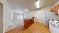 This 2-bedroom, 2-bathroom residence offers a thoughtfully laid-out single-floor design that balances functionality with comfortable living. The open-concept kitchen flows seamlessly into the living area, anchored by a peninsula with a double sink, warm wood-toned cabinetry, laminate countertops, and white appliances including a refrigerator, range, microwave, and dishwasher. Light wood-style flooring extends throughout the kitchen and main areas, transitioning to plush carpet in the living room and bedrooms, creating a cozy, cohesive feel throughout.

The living area is generously proportioned and benefits from natural light streaming through multiple windows, with a ceiling fan adding comfort. The primary bedroom is a well-sized retreat featuring vaulted ceilings, a ceiling fan, large windows with garden views, and direct access to a private en-suite bathroom complete with a walk-in shower and a dedicated walk-in closet. The second bedroom is bright and carpeted, with large windows overlooking a balcony and tree-lined surroundings. The second bathroom features a shower-tub combination, wood-style flooring, a vanity, and cabinet storage. Two closets and a hallway complete the efficient floor plan, providing ample storage throughout the home.