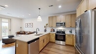 This thoughtfully designed one-bedroom, one-bathroom residence offers a comfortable and functional layout across a single floor. The open-concept living and kitchen area serves as the heart of the home, where warm light wood cabinetry, white quartz countertops, and a full suite of stainless steel Whirlpool appliances — including a refrigerator, range, microwave, and dishwasher — come together seamlessly. A peninsula with bar seating and a pendant light above adds a social dimension to the kitchen, while light hardwood-style flooring runs consistently throughout the entire space, contributing to a cohesive and modern aesthetic. The living room provides an inviting retreat, featuring clean white walls that offer a neutral backdrop. The bedroom is a comfortable, well-proportioned room with the same warm flooring and bright white walls, and connects to a spacious walk-in closet outfitted with wire shelving and hanging rods on multiple walls. The bathroom features a light wood vanity with an undermount sink, white quartz countertop, a large mirror, and crisp white walls. A dedicated laundry room houses a full-size side-by-side washer and dryer. The unit also includes a private balcony, providing an outdoor extension of the living space.
