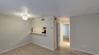This single-floor unit offers a practical and comfortable layout with a variety of flooring and finishes throughout. The open living area is finished with light wood-look laminate flooring and neutral gray walls, creating a clean and versatile canvas. A textured popcorn ceiling adds a classic touch, while a hallway connects the main living space to the rest of the unit. The kitchen is efficiently designed, featuring white cabinetry, speckled laminate countertops, a black electric range with an overhead vent hood, and a sink with ample counter space on either side. The bedroom is a well-proportioned room finished with plush carpet flooring, soft neutral walls, and a ceiling fan with a light fixture to ensure year-round comfort. A window dressed with blinds allows natural light to filter in. The bathroom is clean and functional, offering a full tub and shower combination with tiled surround, a toilet, a wall-mounted towel bar, and a vanity with a speckled countertop and mirror. The overall ambiance of the space is light, neutral, and move-in ready, with consistent finishes that offer a cohesive and comfortable living environment.
