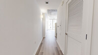 Located at 815 S Hope Street in downtown Los Angeles, this single-floor unit offers a well-organized layout that makes efficient use of its footprint. The space is defined by a striking contrast between crisp white walls and an exposed concrete ceiling, which lends an industrial character to the open living area. A ceiling fan is mounted overhead, adding both function and visual interest to the room.

Light wood-tone flooring runs throughout, contributing to a clean, contemporary aesthetic. Large floor-to-ceiling windows in the living area allow abundant natural light to pour in, offering views of the surrounding downtown Los Angeles skyline. A wide entryway hallway leads into the main living space, which flows directly into the kitchen.

The kitchen features dark wood cabinetry with brushed metal hardware, white countertops, a tile backsplash, and a full suite of stainless steel appliances including a refrigerator, range, microwave, and dishwasher. The layout is efficient and well-appointed for everyday use.

The bathroom includes a soaking tub with an overhead shower, framed by large-format neutral tile on the walls, complemented by chrome fixtures and wood-tone flooring that maintains consistency with the rest of the unit. The overall ambiance is modern and urban.