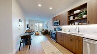 Located on West Colfax Avenue in Denver, this well-appointed one-bedroom, one-bathroom residence offers a thoughtfully designed open-concept layout with modern finishes throughout. Light wood-tone flooring runs continuously across the space, lending warmth and visual cohesion from entry to living area.

The kitchen is a standout feature, showcasing rich walnut-toned cabinetry paired with a white subway tile backsplash, white countertops, and a full suite of stainless steel appliances including a range, microwave, dishwasher, and refrigerator. Open shelving adds both function and style.

The open living and dining area flows seamlessly from the kitchen, benefiting from natural light and direct access to a private balcony through a glass-paned door. The living space offers a comfortable, airy atmosphere with clean white walls and recessed lighting.

The bedroom is generously sized, featuring large windows that invite abundant natural light and views of the surrounding neighborhood. Two closets provide ample storage. The hallway connects the bedroom to the full bathroom, which features a floating walnut vanity with a white countertop, a glass-enclosed walk-in shower with light tile surround and matte black fixtures, and wood-look flooring. A utility room and hallway complete the layout.