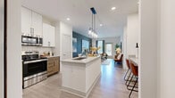 This thoughtfully designed one-bedroom, three-bathroom residence in Terrell, Texas offers a seamless blend of modern aesthetics and functional living. The open-concept kitchen, dining, and living area serves as the heart of the home, anchored by a granite-topped center island with an undermount sink and pendant lighting overhead. The kitchen is outfitted with stainless steel appliances, two-tone cabinetry featuring white upper cabinets and warm wood lower cabinets, a classic subway tile backsplash, and durable light-wood luxury vinyl plank flooring that extends throughout the main living areas. A bold teal accent wall adds a striking visual focal point as the space transitions into the living room, which benefits from natural light through large windows. The primary bedroom features plush carpeting, a ceiling fan, a dedicated accent wall in deep green, and access to a generous walk-in closet with built-in shelving and hanging rods. The bathrooms showcase marble-look tile surrounds with a soaking tub and built-in niche shelving. An elegantly styled entry area with arched mirror detailing completes this well-appointed residence.