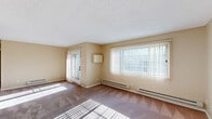 This single-floor residence offers a functional and comfortable layout spread across several well-defined rooms. The living area is generously proportioned, featuring wall-to-wall carpeting, warm beige-toned walls, a textured ceiling, and a large picture window fitted with vertical blinds that allows abundant natural light to fill the space. A glass-paneled door provides additional access and further enhances the brightness of the room. Baseboard heating units are positioned along the exterior walls throughout the unit, ensuring consistent warmth.

The kitchen is designed in a galley configuration, featuring white cabinetry with ample storage, laminate countertops, wood-look vinyl flooring, and white appliances including a range, built-in microwave, and refrigerator. A dedicated laundry room off the kitchen houses a full-size washer and dryer alongside overhead cabinetry for additional storage.

The bedrooms are carpeted and offer generous dimensions, each benefiting from natural light and baseboard heating. One bedroom features dual sets of sliding panel closets, providing exceptional storage capacity. The full bathroom includes a tub-shower combination with tile surround, a vanity with countertop sink, and wood-look vinyl flooring, maintaining the unit's cohesive neutral aesthetic throughout.