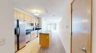 Located at 5630 W 36th St in St. Louis Park, MN, this single-floor unit offers a thoughtfully designed open-concept layout that efficiently combines the kitchen and living areas into one cohesive space. The kitchen is outfitted with stainless steel appliances, including a side-by-side refrigerator with an ice maker, electric range, built-in microwave, and dishwasher. Light maple cabinetry provides generous storage, while dark countertops offer a clean visual contrast. A kitchen island with a matching dark countertop and pendant lighting overhead adds functional prep space and defines the transition between the kitchen and living areas. Hardwood flooring runs throughout the kitchen, giving way to plush carpet in the living area. The living room is notably bright, benefiting from large floor-to-ceiling sliding glass doors that open onto a private balcony, allowing natural light to fill the space and providing outdoor views of the surrounding neighborhood. The bathroom features tile flooring, a tub-shower combination with sliding glass doors, a wood-toned vanity, and built-in cabinetry for additional storage. Overall, the unit presents a clean, modern aesthetic with a practical and comfortable layout.