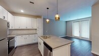 Located at 110 N Chestnut St in Olathe, Kansas, this single-floor residence offers a thoughtfully designed layout with modern finishes throughout. The open-concept kitchen serves as a central feature of the living space, showcasing white shaker-style cabinetry, a classic subway tile backsplash, quartz countertops, and a full suite of stainless steel appliances including a refrigerator, range, microwave, and dishwasher. A kitchen island with an undermount sink provides additional workspace and doubles as a casual dining or gathering area, illuminated by stylish amber pendant lights. The kitchen flows seamlessly into the living area, which features durable wood-look plank flooring, neutral-toned walls, and access to a windowed entry door that invites natural light into the space.

The bedrooms are carpeted for comfort and feature large windows with blinds for natural light control. At least one bedroom includes direct access to a walk-in closet with built-in shelving. The bathroom is well-appointed with a white vanity, quartz countertop, a large mirror, dark hardware accents, and a tiled tub-shower combination. Overall, the unit presents a clean, contemporary aesthetic with consistent finishes that create a cohesive and functional living environment.