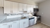Located at 74 Crawford Street in Eatontown, NJ, this 2-bedroom, 1-bathroom unit offers a well-organized single-floor layout designed for comfortable everyday living. The updated kitchen is a standout feature, showcasing crisp white shaker cabinetry, granite countertops, a mosaic tile backsplash, and a full suite of stainless steel appliances including a refrigerator, electric range, microwave, and dishwasher. Light hardwood-style vinyl flooring runs through the kitchen and living areas, while a ceiling fan adds comfort to the open kitchen-dining space. The living room features the same light flooring, a window for natural light, and a baseboard heating system. Both bedrooms are generously sized, each benefiting from multiple windows with blinds that allow ample natural light, along with plush carpeting and baseboard heating. The bathroom is neatly appointed with white tile walls accented by decorative horizontal banding, a tub-shower combination, and dark wood-look tile flooring. Neutral gray tones throughout the unit create a clean, cohesive aesthetic. The 3D floor plan reveals a practical layout with well-connected living spaces, making this a functional and attractive residence in Eatontown.