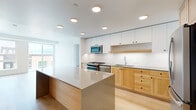 This well-designed two-bedroom, two-bathroom unit offers a thoughtfully arranged single-level floor plan with a clean, modern aesthetic throughout. Light hardwood flooring runs continuously across the entire space, lending warmth and visual cohesion to every room.

The open-concept kitchen and living area serves as the heart of the unit. The kitchen features a two-tone design, pairing white upper cabinetry with natural light wood lower cabinets and drawers. A large central island with a sleek quartz-style countertop provides additional prep space and casual seating. Stainless steel appliances, including a gas range, built-in microwave, and refrigerator, complete the setup, while recessed ceiling lighting illuminates the space effectively.

The living area benefits from large sliding glass doors and adjacent windows that frame outdoor urban views and invite abundant natural light. Both bedrooms are bright and well-proportioned, each with windows offering city views. The primary bedroom includes a dedicated closet with built-in shelving and hanging rods. The bathrooms feature wood vanities with stone-toned countertops and tiled shower surrounds, maintaining the unit's consistent modern palette throughout.