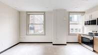 Located on the fifth floor at 929 Walnut St in the heart of Kansas City, MO, this efficiently designed studio unit offers a thoughtfully organized single-floor layout. The open living area is bathed in natural light from two large, classic double-hung windows that frame views of the surrounding downtown cityscape, creating a bright and airy atmosphere throughout.

The kitchen is a functional highlight of the space, featuring a clean, contemporary design with a mix of white upper cabinets and warm wood-toned lower cabinetry, accented by sleek black hardware. Stainless steel appliances — including a range, microwave, and dishwasher — are complemented by a full-size refrigerator, a single-basin sink, and a window that brings additional natural light into the cooking area.

The bathroom offers a minimalist aesthetic with a warm wood vanity, light countertop, modern black fixtures, and a combined shower and tub area with a curtain rod, all finished with neutral, easy-to-maintain surfaces.

Throughout the unit, light-toned flooring and crisp white walls with dark baseboards contribute to a clean, modern feel. An electrical panel and smart home control panel are neatly integrated near the entryway, adding practicality to the space's overall design.