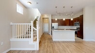 Located at 10207 Dwell Court in Orlando, FL, this two-story home offers 3 bedrooms, 4 bathrooms, and three closets thoughtfully distributed across both floors. The main level features an open-concept kitchen and living area with light hardwood-style flooring throughout. The kitchen is well-appointed with rich dark wood cabinetry, granite countertops, stainless steel appliances including a refrigerator with ice maker, electric range, and built-in microwave, complemented by tile flooring and a classic subway tile backsplash. Pendant lighting and a track light fixture above the island add a stylish touch. A graceful staircase with white balusters and carpeted treads connects the two floors. The living area features a sliding glass door that invites natural light and outdoor access. Upstairs, the bedrooms are carpeted and include vaulted ceilings and walk-in closets with wire shelving. The primary bedroom is comfortably sized with its own closet and natural light from a window. The four bathrooms are clean and functional, each featuring tiled tub-shower combinations, granite-topped dark wood vanities, and tile flooring. Hallways on both levels provide smooth circulation throughout the home.