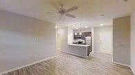 Unit 204 is a 1-bedroom, 1-bathroom residence designed with a clean, modern aesthetic and a thoughtfully open floor plan. The living area is bright and welcoming, featuring light wood-style flooring that runs throughout the space, neutral gray walls, and a ceiling fan that adds both style and comfort. Recessed lighting provides consistent illumination across the open layout.

The kitchen is a standout feature, anchored by a peninsula with a light countertop that serves as both a prep surface and a casual dining or gathering spot. Dark cabinetry contrasts elegantly with the bright countertops, while stainless steel appliances — including a refrigerator, microwave, and range — lend a contemporary, polished feel. Pendant lighting hangs above the peninsula, adding a warm, inviting glow to the space.

The open-concept design seamlessly connects the kitchen to the living area, creating a spacious and functional flow ideal for everyday living and entertaining. A hallway leads to the private bedroom and bathroom, offering a comfortable separation between living and sleeping spaces. The entry door is conveniently positioned, providing easy access to the unit. Overall, the space combines modern finishes with practical design for comfortable, stylish living.