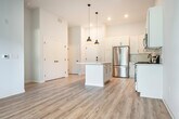 Located at 9411 Modern Pt Ln in Verona, WI, this thoughtfully designed one-bedroom, one-bathroom unit offers a clean, contemporary aesthetic throughout. Light-toned luxury vinyl plank flooring flows seamlessly across the open-concept living, dining, and kitchen areas, creating a cohesive and bright atmosphere enhanced by soaring ceilings that amplify the sense of space.

The kitchen is a standout feature, outfitted with white shaker cabinetry, a white subway tile backsplash, a light quartz countertop island, and a full suite of stainless steel appliances including a refrigerator, gas range, dishwasher, and microwave. Matte black pendant lights hang above the island, adding a modern contrast to the crisp white palette. The living area benefits from large sliding glass doors that open to a private balcony, offering views of the landscaped community courtyard and pool area.

The bedroom features plush carpeting, elevated ceilings, a ceiling fan, and a large window providing natural light and outdoor views. It includes access to both a closet and the full bathroom. The bathroom is finished with a white shaker vanity, quartz countertop, matte black fixtures, a large mirror, and stylish globe light sconces. A hallway connects all spaces efficiently, completing this well-appointed, move-in-ready unit.
