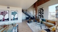 Located at 625 Broadway in the heart of downtown San Diego, this two-story loft masterfully combines industrial heritage with contemporary design. The main level opens into a bright, airy living area defined by soaring ceilings, large windows, and signature exposed brick columns that flood the space with natural light and panoramic city views. Light wood flooring flows throughout, complementing the clean white walls and raw architectural details.

The modern kitchen is a standout feature, offering sleek flat-front cabinetry, stainless steel appliances, a central island with bar seating, and a window framing striking skyline views. A galley-style prep area provides additional counter and storage space alongside the main kitchen. A well-appointed bathroom on the main level includes a combined tub and shower, wood-toned vanity cabinetry, and a large mirror.

Upstairs, the bedroom loft is an intimate retreat surrounded by exposed brick walls, painted structural beams, and industrial pipe details overhead. A metal railing overlooks the lower level, reinforcing the open, connected feel of the two-floor layout. This unit at 625 Broadway delivers a distinctive urban living experience defined by architectural character, abundant natural light, and expansive San Diego cityscape views.