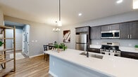 Located at 5510 Southwestern Blvd in Hamburg, NY, this thoughtfully designed single-floor residence offers two bedrooms and two full bathrooms within a comfortable and efficiently laid-out floor plan. The open-concept kitchen, dining, and living area forms the heart of the home, highlighted by a large center island with a white quartz countertop and an undermount sink. Dark-toned shaker-style cabinetry pairs elegantly with stainless steel appliances, while light wood-look flooring runs throughout the main living areas, adding warmth to the cool gray walls. A chandelier over the dining space creates an inviting ambiance for everyday meals. The living room is calm and welcoming, with neutral tones and clean lines. Both bedrooms offer carpeted flooring and natural light from windows with views of the surrounding greenery. The primary bedroom features ample counter space with dark cabinetry and quartz surfaces. The two bathrooms are finished consistently with gray vanities, white quartz countertops, and matte black fixtures — one featuring a walk-in shower with glass enclosure, and the other a tub-shower combination. Clean, modern, and move-in ready, this residence presents a cohesive aesthetic throughout every room.