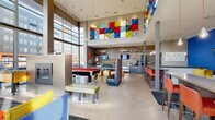 Located in Denver's dynamic RiNo neighborhood, this single-floor community lounge at 3200 Brighton Blvd is a generously sized, open-concept gathering space designed for socializing and recreation. Soaring double-height ceilings and expansive floor-to-ceiling windows on multiple walls flood the interior with abundant natural light while offering views of the surrounding urban streetscape.

The polished concrete flooring anchors the space with an industrial-modern aesthetic, complemented by a reclaimed wood accent wall adorned with decorative fish sculptures and a mounted flat-screen television. A bold, color-blocked art installation spans the upper wall near the main seating area, adding a striking visual focal point alongside additional large-scale artwork throughout.

Distinct zones are thoughtfully arranged within the open layout: a lounge area with soft seating surrounds a sleek double-sided fireplace; a pool table with a red felt surface serves as a central recreational feature; and a bar-height counter set against a vivid cobalt blue accent wall — equipped with pendant lighting and multiple mounted screens — provides a casual workspace or social perch. Additional lounge seating, built-in window benches, and a coffee and refreshment station round out the amenities, creating a multifunctional space suited for relaxation, work, and entertainment.