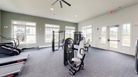 Located at 1120 Corner Wind Ln in Columbia, SC, this well-equipped fitness center offers a generous, open layout designed to accommodate a wide range of workout needs. The space is finished with durable, dark-toned carpet flooring throughout and features crisp white walls accented by sage green paint, creating a clean and energizing atmosphere.

Natural light pours in through numerous large, white-trimmed windows positioned along multiple walls, offering views of the surrounding community and keeping the space feeling open and inviting. Recessed lighting and ceiling fans with integrated lighting fixtures provide additional illumination and airflow throughout the room.

The cardio zone is well-stocked with multiple treadmills and an elliptical trainer, all positioned to face the windows for an engaging workout experience. The strength training area includes a power rack with a barbell system, a cable crossover machine, a variety of selectorized strength machines, adjustable benches, kettlebells, medicine balls, and resistance bands neatly organized on a dedicated storage rack. A large wall-mounted mirror expands the visual depth of the space and supports form monitoring during exercise. The facility also includes a rowing machine, providing a full-body cardio option. Overall, the fitness center is thoughtfully outfitted to support cardiovascular fitness, functional training, and strength development in a bright, community-oriented setting.
