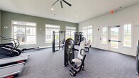 Located at 1120 Corner Wind Ln in Columbia, SC, this well-equipped fitness center offers a generous, open layout designed to accommodate a wide range of workout needs. The space is finished with durable, dark-toned carpet flooring throughout and features crisp white walls accented by sage green paint, creating a clean and energizing atmosphere.

Natural light pours in through numerous large, white-trimmed windows positioned along multiple walls, offering views of the surrounding community and keeping the space feeling open and inviting. Recessed lighting and ceiling fans with integrated lighting fixtures provide additional illumination and airflow throughout the room.

The cardio zone is well-stocked with multiple treadmills and an elliptical trainer, all positioned to face the windows for an engaging workout experience. The strength training area includes a power rack with a barbell system, a cable crossover machine, a variety of selectorized strength machines, adjustable benches, kettlebells, medicine balls, and resistance bands neatly organized on a dedicated storage rack. A large wall-mounted mirror expands the visual depth of the space and supports form monitoring during exercise. The facility also includes a rowing machine, providing a full-body cardio option. Overall, the fitness center is thoughtfully outfitted to support cardiovascular fitness, functional training, and strength development in a bright, community-oriented setting.