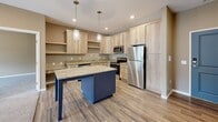 Located at 1130 County Rd in Saint Cloud, MN, this 2-bedroom, 2-bathroom single-floor unit offers a thoughtfully designed layout with modern finishes throughout. The open-concept kitchen and living area serves as the heart of the home, featuring light natural wood cabinetry, granite countertops, a bold navy blue center island with pendant lighting, and a full suite of stainless steel appliances including a refrigerator, range, microwave, and dishwasher. Wood-look luxury vinyl plank flooring runs through the kitchen and transitions to plush carpet in the living and bedroom areas. The living room is anchored by a sleek built-in linear fireplace with a light wood surround and recessed display niche above, complemented by a wall-mounted mini-split unit. The spacious primary bedroom features sliding glass door access to an outdoor view, while the second bedroom is bright with a large window overlooking the surroundings. Both bathrooms are finished with granite-topped wood vanities and tile flooring; one includes a walk-in shower. Warm beige tones carried throughout the unit create a cohesive, inviting ambiance, while recessed lighting and baseboard heating add to the unit's practical comfort.