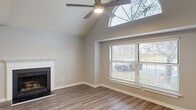 This single-story home is designed with a thoughtful open layout that balances comfortable living with functional spaces. The living room serves as a focal point, showcasing dramatic vaulted ceilings that soar upward and are accentuated by an arched transom window, flooding the space with natural light. A ceiling fan complements the height, while a classic wood-burning fireplace with a white surround adds warmth and character. Large windows with blinds offer views of the surrounding outdoor area, and sliding glass doors provide direct exterior access.

The kitchen is efficiently designed with white cabinetry, granite countertops, and a peninsula that serves as both a prep area and casual dining space. Stainless steel appliances, including a refrigerator, range, and microwave, complete the modern aesthetic.

The bedrooms are well-proportioned, featuring the same durable wood-look flooring found throughout the home and generous natural light from well-placed windows. One bedroom includes direct access to a bathroom and an additional room, likely a closet or secondary space. Both bathrooms are finished with granite vanity surfaces and full tub-shower combinations with brushed nickel fixtures, maintaining a consistent, clean aesthetic throughout.