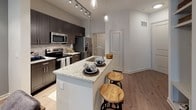 This thoughtfully designed one-bedroom, one-bathroom residence offers a cohesive blend of modern aesthetics and practical functionality across a single floor. The open-concept kitchen serves as a focal point, showcasing dark espresso cabinetry, a tile backsplash, stainless steel appliances, and a granite-topped island with an undermount sink and bar seating—ideal for casual dining or entertaining. Track lighting overhead enhances the kitchen's contemporary appeal. Wood-look flooring flows throughout the main living areas, creating a seamless transition between spaces.

The living room is bright and welcoming, featuring a ceiling fan, a neutral color palette, and direct access to a private outdoor area through a glass door that allows natural light to fill the room. A bold accent wall adds a distinctive design touch to the bedroom, which is carpeted for comfort and includes a ceiling fan. The full bathroom features granite countertops, dark cabinetry consistent with the kitchen, and a tub/shower combination. A dedicated in-unit laundry area with full-size washer and dryer hookups adds everyday convenience, completing this well-rounded residence.