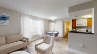 This single-floor residence offers a well-organized layout that balances comfort and functionality. The living area serves as the heart of the unit, finished with wood-look flooring and neutral tones that create a warm, inviting atmosphere. Large windows dressed with vertical blinds allow abundant natural light to fill the space, while a dedicated dining area sits adjacent, providing a seamless transition between relaxation and entertaining.

The galley-style kitchen features warm-toned wood cabinetry, dark countertops, a double sink, dishwasher, and refrigerator. A peninsula counter opens toward the living and dining areas, enhancing the sense of connectivity throughout the common spaces. A hallway off the kitchen provides access to the remaining rooms.

Two bedrooms offer comfortable retreats, each equipped with ceiling fans, wood-look flooring, and windows that invite natural light. The primary bedroom includes a walk-in closet and direct access to a private bathroom. A second bathroom serves the additional bedroom and common areas, featuring a wood-toned vanity and dark countertop. Louvered closet doors and wire shelving provide practical storage solutions. Textured ceilings and neutral wall colors are consistent throughout, contributing to the cohesive, understated character of the space.