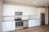 This contemporary single-floor residence offers a thoughtfully designed open-concept layout with a clean, modern aesthetic throughout. The kitchen is a standout feature, showcasing white shaker cabinetry, granite countertops, a white subway tile backsplash, and a full suite of stainless steel appliances including a range, microwave, dishwasher, and refrigerator. Light hardwood flooring runs through the main living areas, lending warmth and continuity to the space.

The living area is generously sized and bathed in natural light, courtesy of expansive floor-to-ceiling windows that frame views of the surrounding streetscape and neighborhood beyond. The bright, airy atmosphere is further enhanced by recessed lighting and a neutral color palette throughout.

The bedrooms are comfortably proportioned, finished with soft carpet flooring, and feature large windows that bring in additional natural light and outdoor views. Closet space is provided in the bedrooms for practical storage.

The bathrooms are finished in a clean, minimalist style with white vanities, wood-look flooring, and a tub-shower combination. A well-proportioned entry hallway connects the spaces efficiently. Overall, the residence presents a fresh, move-in-ready interior with modern finishes and a bright, welcoming ambiance.