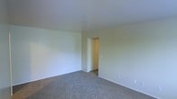 This single-floor space offers a straightforward and functional layout designed for comfortable living. The interior is finished with neutral, light-toned walls that create a bright and airy atmosphere throughout. Soft wall-to-wall carpeting covers the floors, adding warmth and a quiet, comfortable feel underfoot. The room visible in the space is generously sized, providing ample room for furnishing and personalization. A closet is accessible through a dedicated doorway, offering practical built-in storage with a standard hanging rod. The clean white ceiling complements the light walls, contributing to an overall sense of openness. Baseboards run along the perimeter of the room, adding a neat finishing detail. Electrical outlets are conveniently positioned along the walls, accommodating a variety of furniture arrangements. The space is presented in a vacant, move-in-ready condition, allowing prospective occupants to clearly assess its dimensions and layout. The overall design is simple and uncluttered, making it a versatile canvas for a range of interior styles and uses. The single-floor layout ensures easy accessibility and seamless flow between areas of the space.