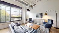 Located at 350 Mount Vernon Ave in Columbus, Ohio, this single-floor loft showcases a compelling blend of industrial character and contemporary design. The open living area commands attention with soaring ceilings, exposed ductwork, and an oversized ceiling fan, all framed by large, multi-pane factory-style windows that flood the space with natural light and offer views of the surrounding greenery. The living room features polished hardwood flooring accented by concrete, complemented by modern décor and geometric wall art that reinforce the loft's urban aesthetic.

The kitchen is outfitted with stainless steel appliances — including a full-size refrigerator, dishwasher, electric range, and microwave — paired with two-tone cabinetry, white subway tile backsplash, and a stainless steel island, delivering both style and functionality. Polished concrete flooring extends throughout the kitchen area.

The bedroom offers a refined retreat centered around a striking four-poster canopy bed frame, with access to a spacious walk-in closet. Two well-appointed bathrooms each feature glass-enclosed walk-in showers with white subway tile surround, modern vanities with dark wood cabinetry, and clean, minimalist finishes. The cohesive design throughout this loft makes it a standout residence in Columbus's vibrant Mount Vernon corridor.