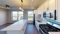 This well-appointed single-floor unit offers a thoughtfully designed open-concept layout that seamlessly connects the living and kitchen areas. The kitchen is a standout feature, showcasing white shaker cabinetry, a subway tile backsplash, a large central island with a white quartz countertop, and a full suite of stainless steel appliances including a gas range, built-in microwave, dishwasher, and French door refrigerator. Track lighting and pendant fixtures illuminate the space, while expansive windows frame urban views and fill the area with natural light. Rich wood-look flooring runs throughout the main living space, adding warmth and continuity.

The unit includes two bedrooms, both finished with plush carpeting and windows overlooking the surrounding neighborhood. The primary bedroom connects to a private en-suite bathroom featuring a wide single-sink vanity with white cabinetry, a large mirror, and stylish fixtures, alongside a spacious walk-in closet with wire shelving. A second full bathroom offers a tub-shower combination, a white vanity, and a modern three-bulb vanity light fixture. Additional highlights include a dedicated in-unit laundry area and ample closet storage throughout. The neutral color palette and clean finishes give the space a fresh, contemporary feel.