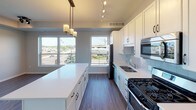 This well-appointed single-floor unit offers a thoughtfully designed open-concept layout that seamlessly connects the living and kitchen areas. The kitchen is a standout feature, showcasing white shaker cabinetry, a subway tile backsplash, a large central island with a white quartz countertop, and a full suite of stainless steel appliances including a gas range, built-in microwave, dishwasher, and French door refrigerator. Track lighting and pendant fixtures illuminate the space, while expansive windows frame urban views and fill the area with natural light. Rich wood-look flooring runs throughout the main living space, adding warmth and continuity.

The unit includes two bedrooms, both finished with plush carpeting and windows overlooking the surrounding neighborhood. The primary bedroom connects to a private en-suite bathroom featuring a wide single-sink vanity with white cabinetry, a large mirror, and stylish fixtures, alongside a spacious walk-in closet with wire shelving. A second full bathroom offers a tub-shower combination, a white vanity, and a modern three-bulb vanity light fixture. Additional highlights include a dedicated in-unit laundry area and ample closet storage throughout. The neutral color palette and clean finishes give the space a fresh, contemporary feel.
