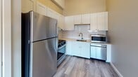 Located at 2908 Smallman Street in Pittsburgh's vibrant Strip District, this single-floor unit blends industrial character with modern updates. Exposed wooden ceiling beams and open ductwork lend a loft-like aesthetic throughout the living areas, complemented by durable light-toned wood-style flooring that runs seamlessly across the space.

The kitchen is well-appointed with white shaker-style cabinetry, a classic subway tile backsplash, and a full suite of stainless steel appliances including a refrigerator, gas range, microwave, and dishwasher. Ample upper and lower cabinet storage makes this kitchen as functional as it is attractive.

The living area is open and airy, benefiting from the soaring ceiling height and a clean, neutral palette that offers a versatile canvas. A dedicated bedroom features an exposed brick wall with a large window framing views of the surrounding neighborhood, bringing in natural light and a sense of urban connectivity.

The bathroom is spacious and thoughtfully designed with accessibility in mind, featuring grab bars, a full tub with shower, and large-format tile flooring that enhances the bright, clean atmosphere. The overall layout, as seen in the 3D model, is efficiently organized and well-suited for comfortable everyday living in one of Pittsburgh's most dynamic neighborhoods.