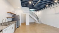 This contemporary 820 square foot property in Tucson, Arizona, showcases a thoughtful blend of form and function across its two floors. The ground level presents an open-concept living area with polished concrete floors, exposed ceiling beams, and track lighting, creating an industrial-chic ambiance. A sleek kitchen area features white cabinetry, stainless steel appliances, and open shelving, ideal for modern living. The space is further enhanced by a striking garage-style door, offering potential for indoor-outdoor flow.

Ascending to the upper level via a modern staircase with metal railings, you'll find additional living space with light wood flooring and recessed lighting. The bathroom boasts a clean, minimalist design with a spacious shower, white tiles, and a floating vanity. Throughout the property, ample windows and glass doors allow natural light to permeate the spaces, while wall-mounted air conditioning units ensure year-round comfort. A dedicated laundry area with stacked appliances adds convenience to this efficiently designed urban dwelling.