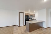 Located at 5730 Leubecher Ave in Sioux Falls, South Dakota, this one-bedroom, one-bathroom unit offers a thoughtfully designed layout that maximizes every square foot of living space. The open-concept living and kitchen area serves as the heart of the unit, where light wood-tone flooring flows seamlessly underfoot. The kitchen is appointed with dark espresso cabinetry, light countertops, a full suite of black appliances including a refrigerator, electric range, and microwave, and a peninsula with a double-basin sink that doubles as a breakfast bar and room divider. The living area features plush carpet and sliding glass doors that lead to a private balcony, inviting natural light deep into the space. The bedroom is comfortably sized with wall-to-wall carpet, a large window with neighborhood views, and direct access to a closet. The bathroom includes a full soaking tub and shower combination with clean white surround. A dedicated in-unit laundry room with side-by-side washer and dryer hookups and overhead shelving adds everyday convenience. The overall aesthetic is clean, neutral, and move-in ready.
