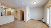 This single-floor unit offers a thoughtfully designed open-concept layout that seamlessly connects the living and kitchen areas. The spacious living room is finished with plush neutral carpeting, warm wood-toned baseboards, and a set of French doors fitted with blinds that invite natural light while providing access to the outdoors. The open layout allows for generous furniture placement and a comfortable sense of scale throughout.

The kitchen is a functional and stylish centerpiece, featuring rich dark-espresso cabinetry that extends to the ceiling for ample storage. A full suite of stainless steel appliances includes a refrigerator, electric range, built-in microwave, and dishwasher. Light hardwood-style flooring, a double-basin sink, and a raised breakfast bar with pendant lighting complete the space.

A half-wall partition neatly separates the kitchen from the living area, maintaining the open feel while defining each zone. Additional interior doors lead to a private bedroom area and closet spaces. The bathroom is clean and practical, offering a full tub-shower surround, tile flooring, a vanity with a white countertop, and dark cabinetry consistent with the kitchen's design language. Overall, the unit presents a cohesive, modern aesthetic with neutral tones throughout.