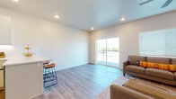 This single-floor space showcases a contemporary design with a bright, open-concept layout connecting the living, dining, and kitchen areas. Light-toned wood-style flooring runs throughout the main living spaces, contributing to a clean, cohesive aesthetic. Recessed lighting and a ceiling fan enhance the airy feel of the living area, which benefits from natural light provided by a sliding glass door leading to a private balcony. The living room offers ample space for seating and includes a window with blinds for additional light control.

The kitchen is well-equipped with white shaker-style cabinetry, white quartz countertops, a classic subway tile backsplash, and stainless steel appliances including a range and over-the-range microwave. A peninsula with bar seating provides a functional space for casual dining or meal prep.

The full bathroom features large-format tile surrounding a soaking tub and shower combination, a white vanity with quartz countertops, and modern fixtures. A secondary bathroom with a compact vanity and toilet is also present. The bedroom is carpeted for comfort and includes a ceiling fan and window with blinds, creating a quiet, restful environment.