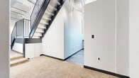 Located in the heart of downtown Frederick, Maryland, this two-floor urban unit at 15 W Patrick St offers a compelling blend of industrial-loft aesthetics and modern finishes. The main floor features open, carpeted living areas bathed in natural light through large black-framed windows that frame views of the surrounding cityscape. Exposed ductwork, concrete ceiling beams, and track lighting run throughout, reinforcing the loft-inspired character of the space. A sleek black metal staircase connects the floors, adding a bold architectural focal point. The hallway transitions seamlessly between areas with tile flooring, providing a practical contrast to the plush carpet in the main rooms. The bathroom is a standout feature, showcasing a jetted soaking tub, a glass-enclosed walk-in shower, and white tile accented with striking blue border detail — all topped with a dramatic ceiling detail and served by natural light from windows overlooking the city. Upper-level access leads to a private rooftop deck finished with warm wood decking, a built-in grill, seating area, and panoramic views of Frederick's skyline and the surrounding mountains — an exceptional outdoor amenity. Built-in shelving and thoughtful storage solutions add functional value throughout this distinctive urban space.