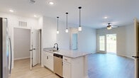 Located at 500 Legends Dr in Southern Pines, NC, this well-appointed 2-bedroom, 2-bathroom single-floor home offers a thoughtfully designed layout with modern finishes throughout. Light-toned hardwood-style flooring runs consistently across all rooms, lending a clean, cohesive aesthetic to the entire space.

The open-concept kitchen and living area serves as the heart of the home. The kitchen features white cabinetry, granite countertops, a peninsula with an undermount sink and matte black faucet, stainless steel appliances including a refrigerator, range, microwave, and dishwasher, and three stylish pendant lights overhead. The adjacent living room is bright and airy, with a ceiling fan and a door leading to an outdoor balcony with scenic green views.

The dedicated dining room is highlighted by elegant wainscoting along the lower walls and a contemporary chandelier, adding a refined architectural detail to the space.

The spacious primary bedroom includes a ceiling fan and connects to a well-sized en-suite bathroom featuring a dual-sink vanity with granite countertops, a large framed mirror, and a glass-enclosed shower. The second bedroom is comfortably sized with its own ceiling fan. Additional conveniences include a dedicated laundry room with wire shelving and washer/dryer hookups, a hallway, and a closet.